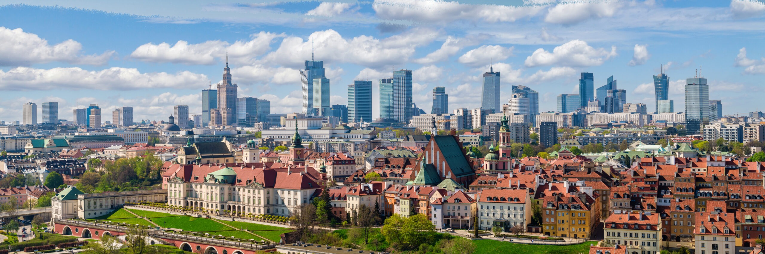 Obrazek przedstawiający panoramę Starego Miasta w Warszawie i odległe centrum miasta z wieżowcami i Pałacem Kultury i Nauki, pod błękitnym, zachmurzonym niebem. Obraz symbolizujący połączenie tradycji z nowoczesnością i całościowe spojrzenie na zarządzanie aktywami.